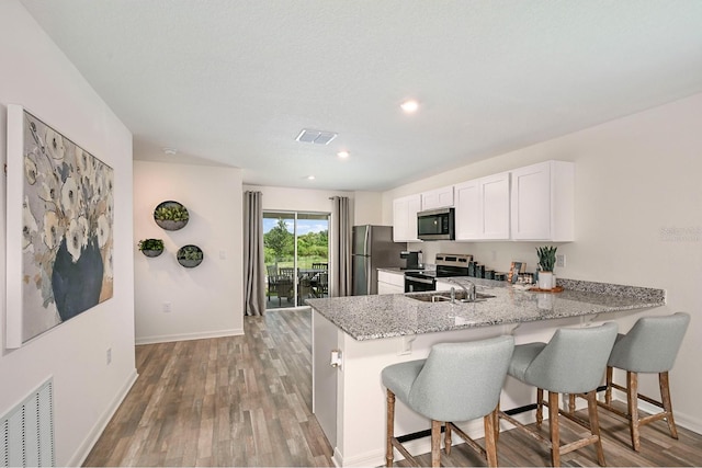 kitchen with light hardwood / wood-style floors, white cabinetry, light stone counters, kitchen peninsula, and stainless steel appliances