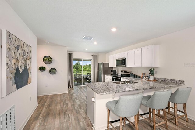 kitchen featuring a kitchen bar, light stone counters, kitchen peninsula, stainless steel appliances, and white cabinets