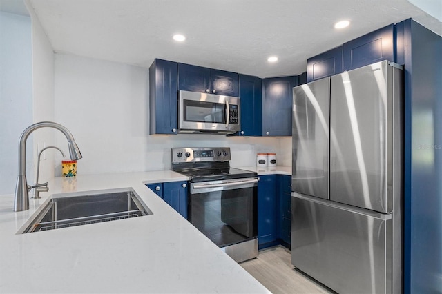 kitchen with appliances with stainless steel finishes, blue cabinetry, sink, and light wood-type flooring