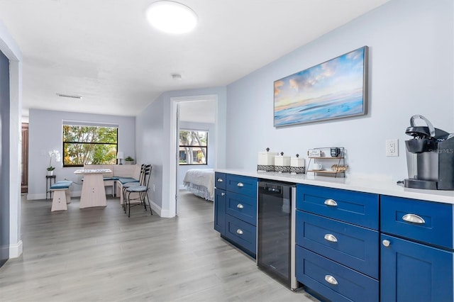 bar with light hardwood / wood-style flooring, blue cabinets, and beverage cooler