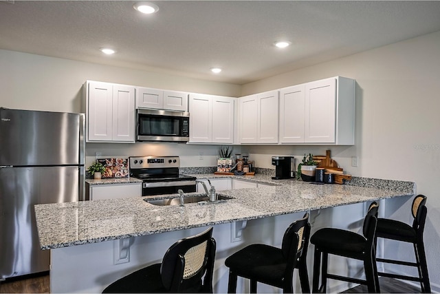 kitchen featuring appliances with stainless steel finishes, kitchen peninsula, white cabinetry, and sink