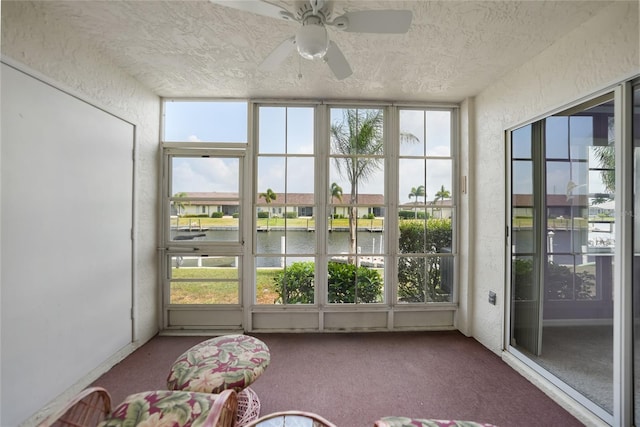 unfurnished sunroom featuring ceiling fan and a water view