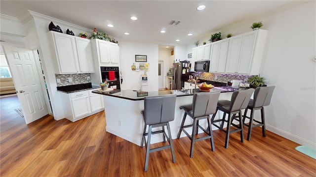 kitchen featuring a kitchen breakfast bar, black appliances, hardwood / wood-style floors, kitchen peninsula, and white cabinets