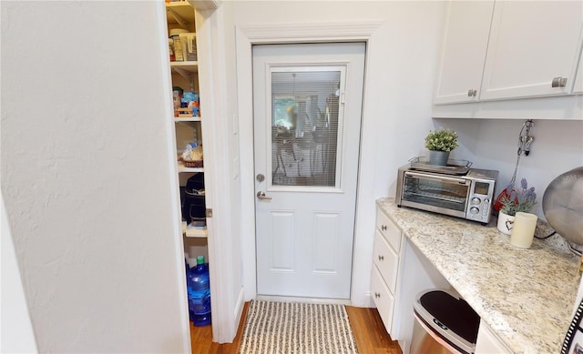 kitchen with built in desk, hardwood / wood-style flooring, light stone counters, and white cabinetry