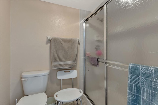 bathroom featuring a shower with door and toilet