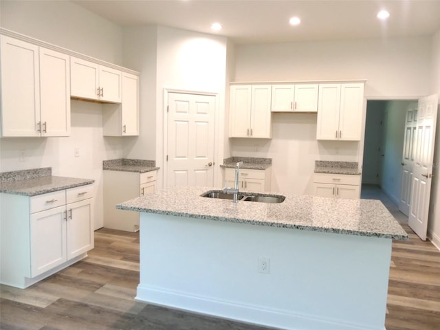 kitchen with a kitchen island with sink, white cabinets, sink, light stone counters, and wood-type flooring