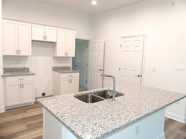 kitchen featuring white cabinetry, a kitchen island with sink, light hardwood / wood-style flooring, and light stone counters