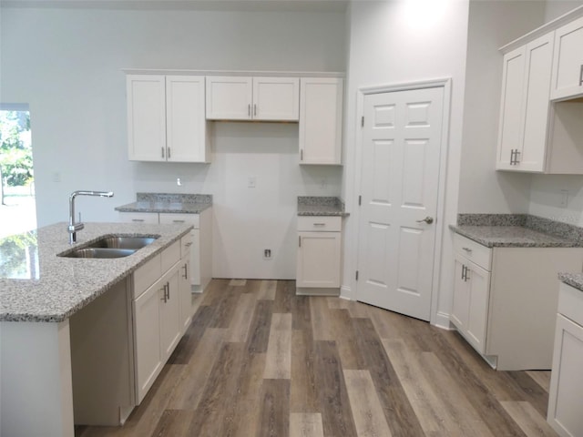 kitchen featuring light stone countertops, light hardwood / wood-style flooring, white cabinetry, and sink