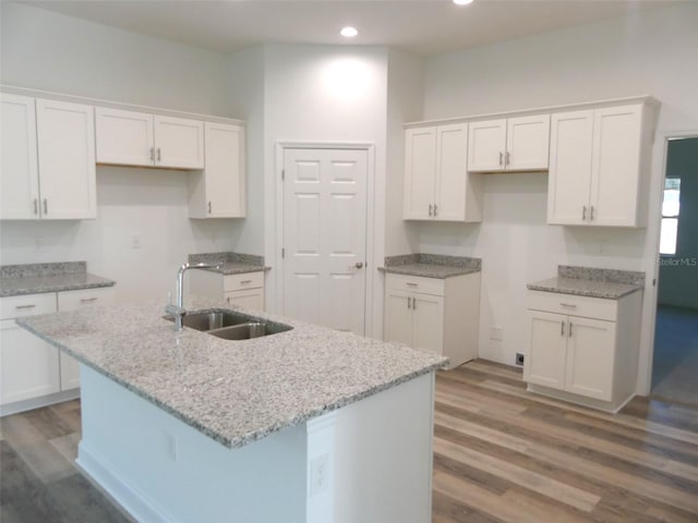 kitchen with white cabinetry, sink, light stone countertops, hardwood / wood-style floors, and a kitchen island with sink