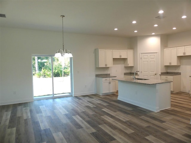 kitchen featuring light stone countertops, dark wood-type flooring, sink, a center island with sink, and white cabinetry