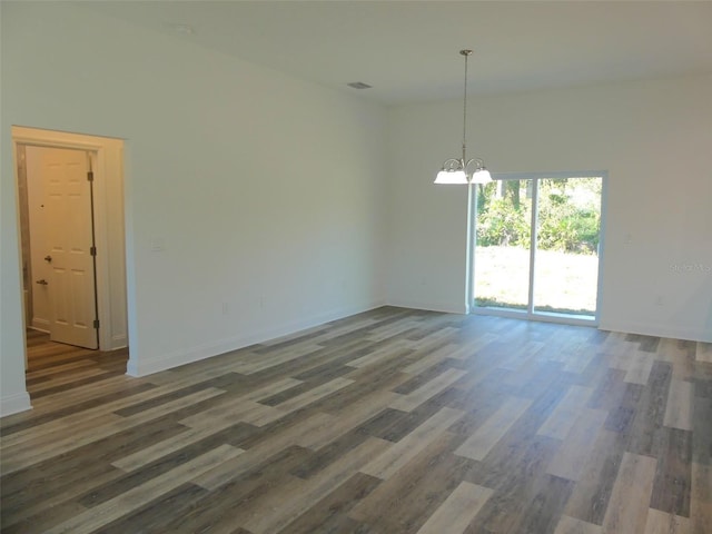 spare room featuring dark wood-type flooring and a notable chandelier