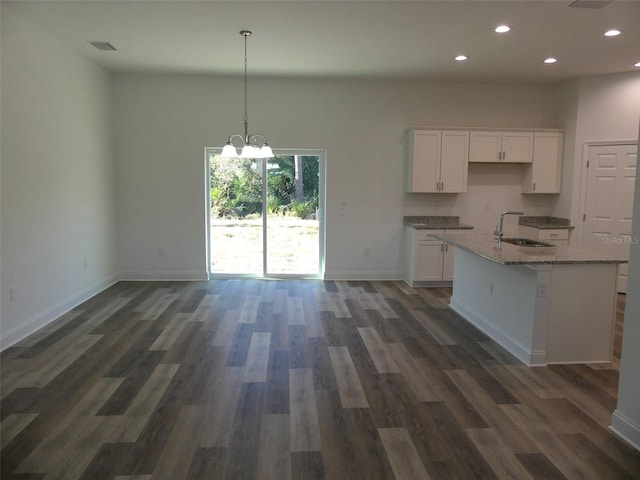 kitchen featuring light stone counters, dark hardwood / wood-style floors, pendant lighting, a kitchen island with sink, and white cabinets