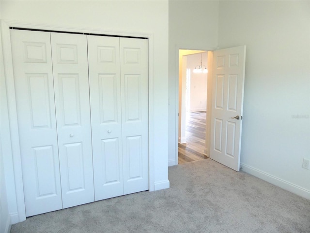 unfurnished bedroom featuring a closet, light colored carpet, and a notable chandelier