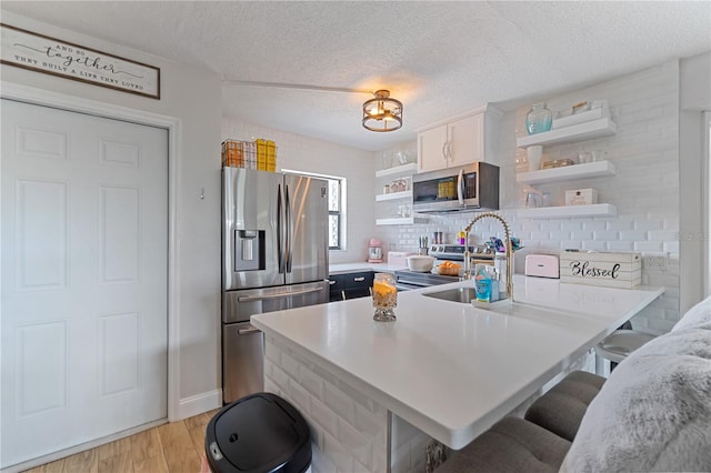 kitchen with sink, light hardwood / wood-style floors, a textured ceiling, a breakfast bar, and appliances with stainless steel finishes