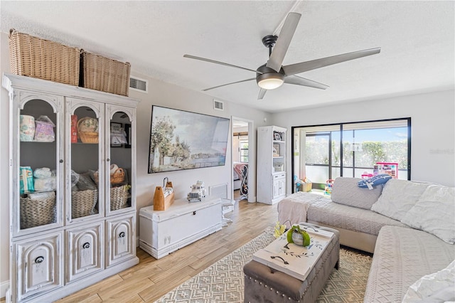 living room with a textured ceiling, light hardwood / wood-style flooring, and ceiling fan