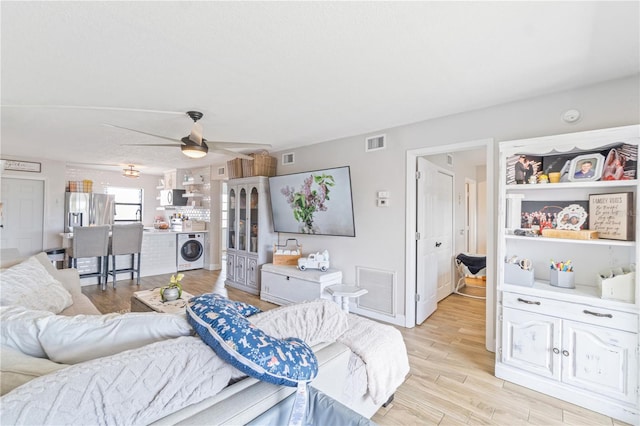 living room with washer / clothes dryer, ceiling fan, and light hardwood / wood-style floors