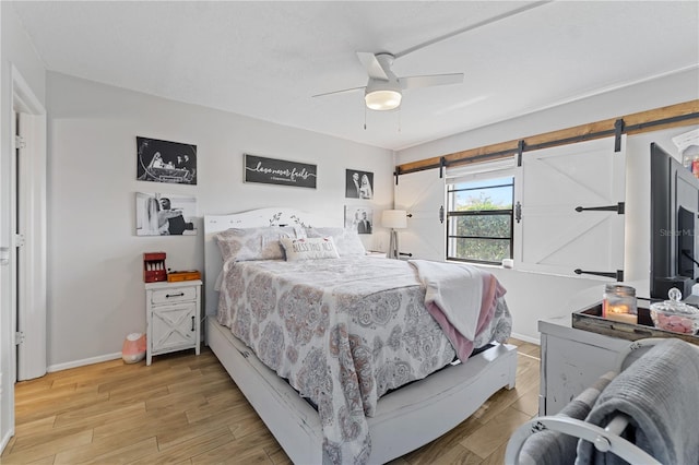 bedroom with a barn door, ceiling fan, and light hardwood / wood-style floors