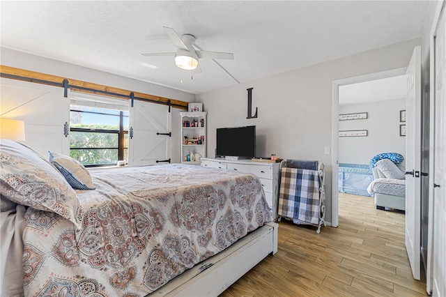 bedroom with a barn door, ceiling fan, and light hardwood / wood-style floors