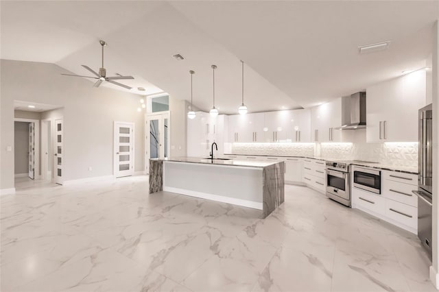 kitchen with a kitchen island with sink, white cabinets, vaulted ceiling, wall chimney exhaust hood, and decorative light fixtures