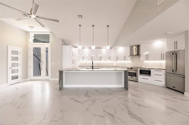 kitchen with stainless steel appliances, ceiling fan, wall chimney range hood, white cabinets, and hanging light fixtures