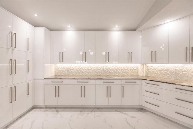 kitchen featuring white cabinets, decorative backsplash, light stone countertops, and lofted ceiling