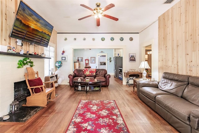 living room with wooden walls, wood-type flooring, and ceiling fan