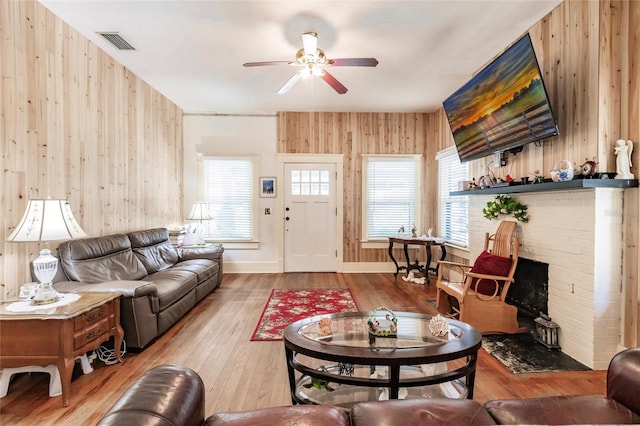 living room featuring wood-type flooring, wooden walls, and ceiling fan