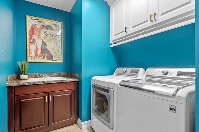 clothes washing area with washing machine and dryer, sink, and cabinets