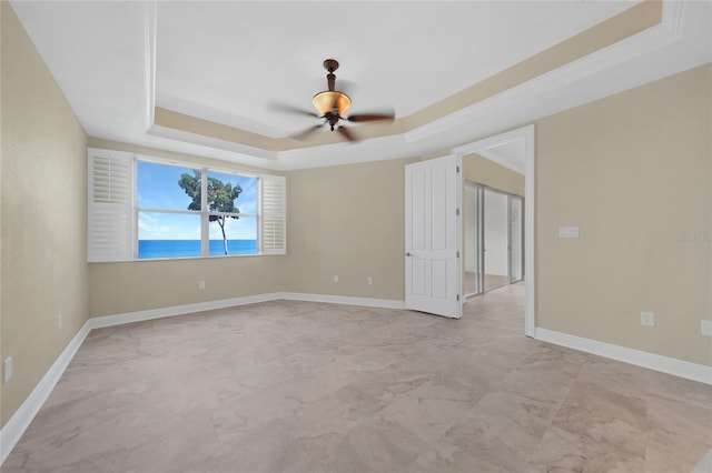 empty room with ceiling fan, a raised ceiling, and tile floors