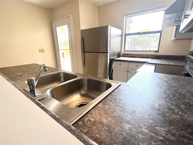 kitchen with plenty of natural light, white cabinets, stainless steel fridge, and range