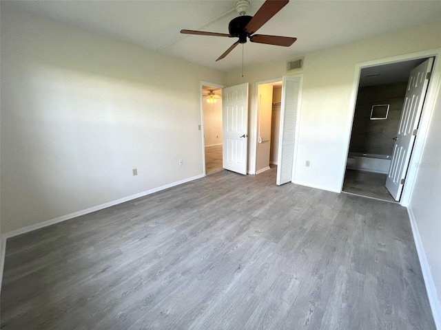 unfurnished bedroom with ensuite bath, ceiling fan, dark wood-type flooring, and a closet