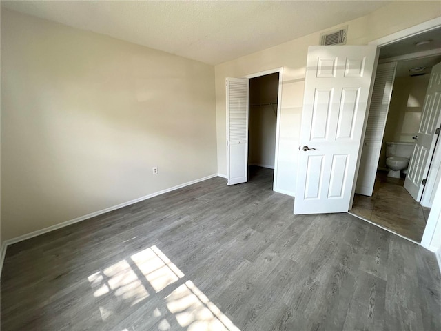 unfurnished bedroom with a closet, hardwood / wood-style floors, and ensuite bathroom