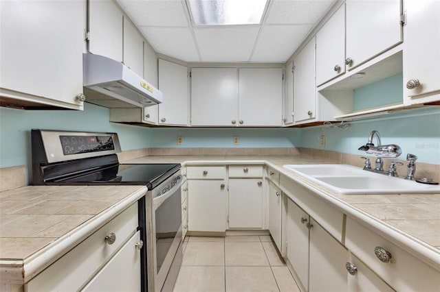 kitchen featuring electric stove, sink, light tile patterned floors, tile counters, and white cabinetry