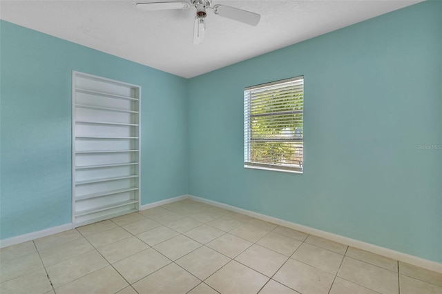 tiled spare room featuring built in shelves and ceiling fan