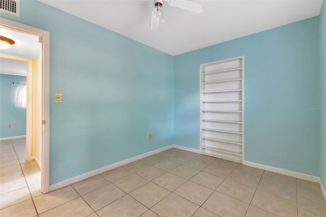 empty room with built in shelves, light tile patterned floors, and ceiling fan