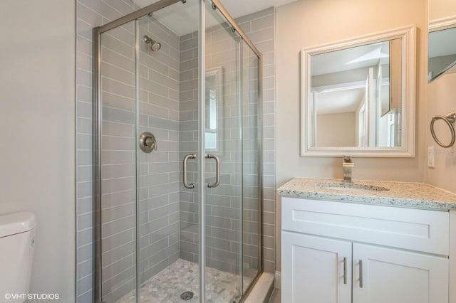 bathroom featuring a shower with shower door, toilet, and vanity