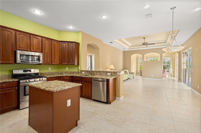 kitchen featuring decorative light fixtures, kitchen peninsula, stainless steel appliances, a tray ceiling, and sink