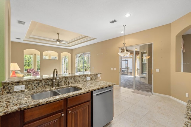 kitchen with a tray ceiling, stainless steel dishwasher, sink, light tile floors, and pendant lighting