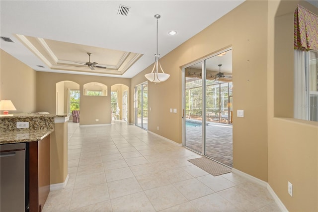 kitchen featuring a raised ceiling, light stone countertops, ceiling fan, and decorative light fixtures