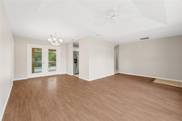 unfurnished living room featuring a tray ceiling, french doors, ceiling fan with notable chandelier, and light hardwood / wood-style flooring