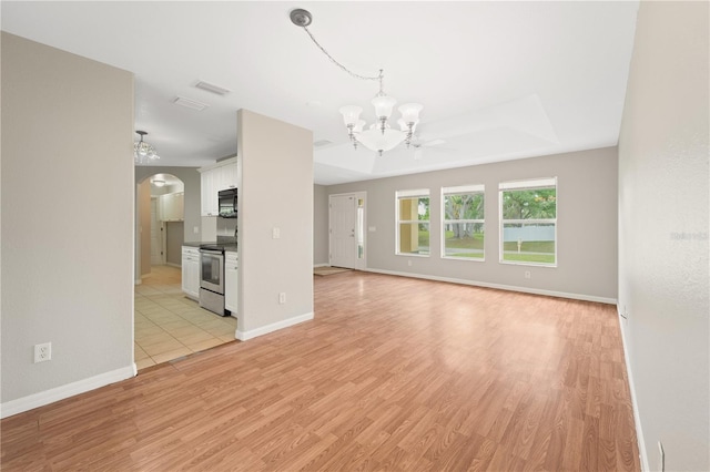 unfurnished living room with a raised ceiling, ceiling fan with notable chandelier, and light wood-type flooring