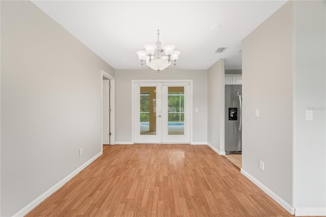 unfurnished dining area featuring light hardwood / wood-style floors, french doors, and a chandelier