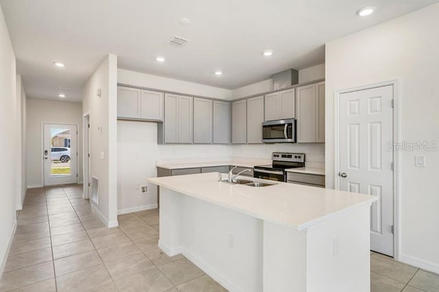 kitchen with gray cabinetry, an island with sink, appliances with stainless steel finishes, sink, and light tile floors