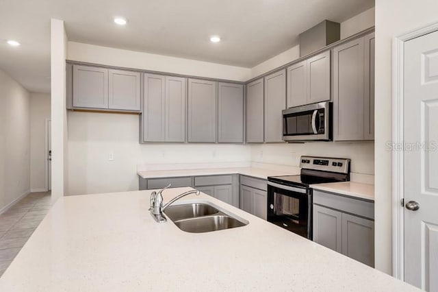 kitchen with light stone counters, gray cabinetry, appliances with stainless steel finishes, sink, and light tile floors