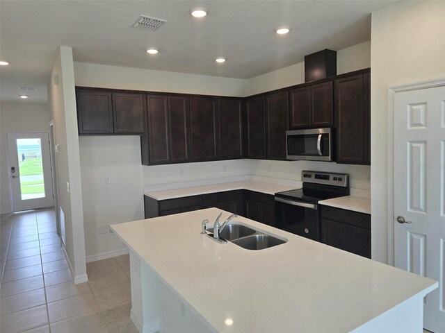 kitchen with dark brown cabinets, stainless steel appliances, light tile flooring, sink, and a kitchen island with sink