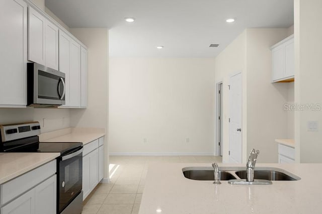 kitchen featuring appliances with stainless steel finishes, sink, white cabinets, and light tile flooring