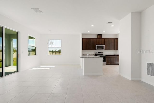 kitchen with appliances with stainless steel finishes, a kitchen island with sink, dark brown cabinets, pendant lighting, and light tile floors