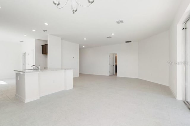 kitchen featuring light stone countertops, a kitchen island with sink, dark brown cabinets, sink, and light tile floors