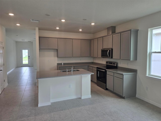 kitchen with stainless steel appliances, an island with sink, gray cabinets, sink, and light tile floors