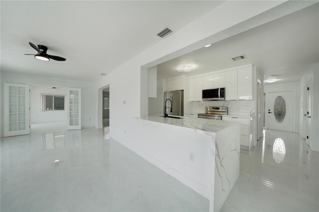 kitchen with light stone countertops, ceiling fan, stainless steel appliances, sink, and white cabinetry